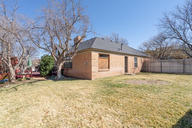 back of house featuring a yard, fence, brick siding, and a chimney