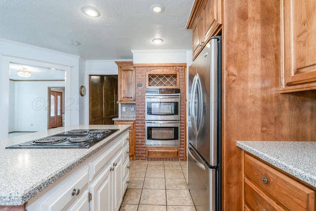 kitchen with crown molding, brown cabinets, appliances with stainless steel finishes, light tile patterned flooring, and white cabinets