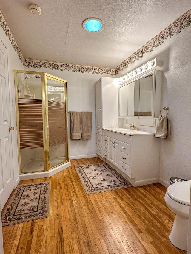 bathroom featuring hardwood / wood-style floors, vanity, a textured ceiling, a shower with shower door, and toilet