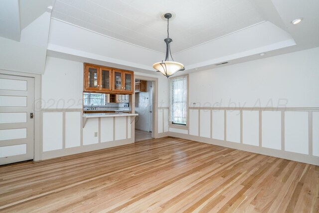 2523 5th Ave, Canyon, TX 79015 - kitchen with light wood-type flooring, a tray ceiling, glass insert cabinets, a peninsula, and plenty of natural light