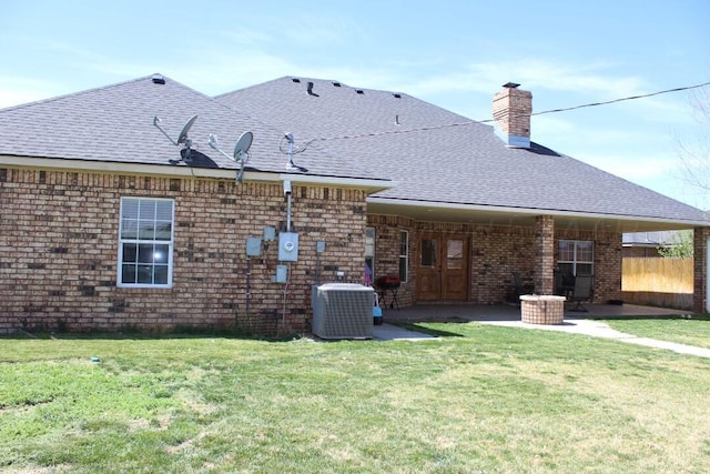 rear view of house with cooling unit, a lawn, a shingled roof, and a patio