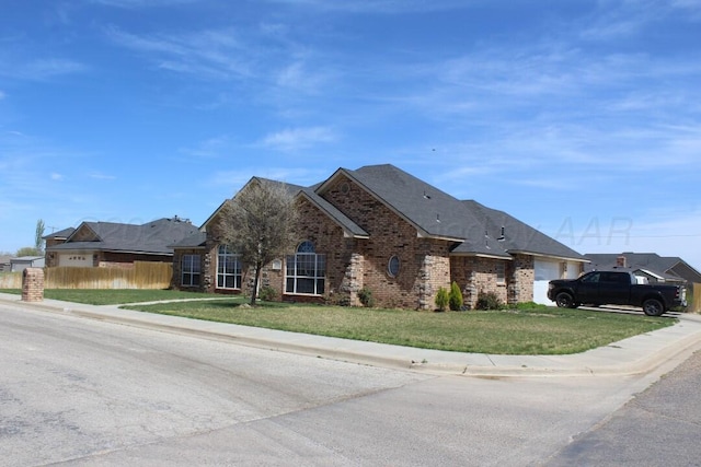 view of front facade featuring brick siding, a garage, a front lawn, and fence