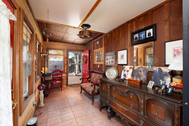 sitting room with ornamental molding, wooden walls, and light tile patterned floors