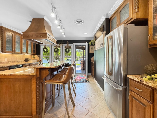 120 Port O Call Dr, Amarillo, TX 79118 - kitchen with freestanding refrigerator, custom range hood, light tile patterned flooring, brown cabinetry, and backsplash