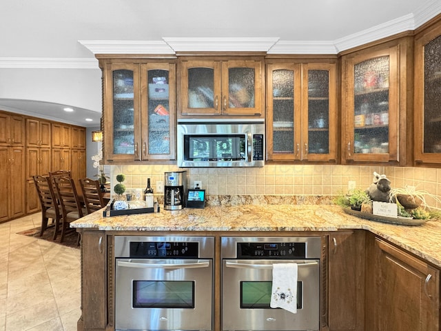 120 Port O Call Dr, Amarillo, TX 79118 - kitchen with stainless steel appliances, crown molding, backsplash, light stone countertops, and brown cabinetry