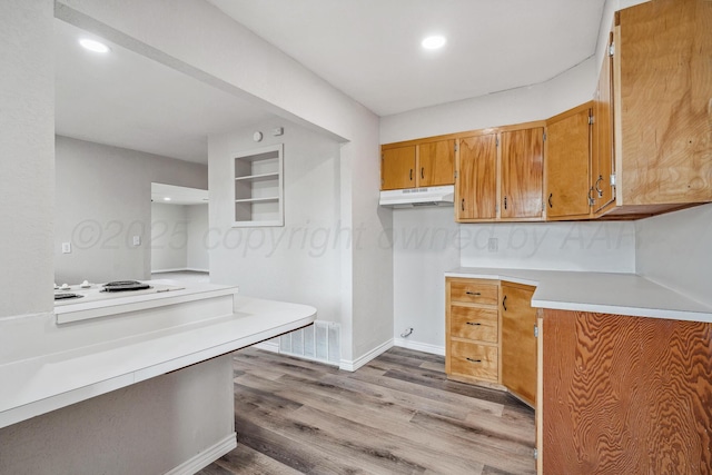 517 Whittier St, Hereford, TX 79045 - kitchen with under cabinet range hood, light countertops, light wood-type flooring, brown cabinetry, and white electric cooktop