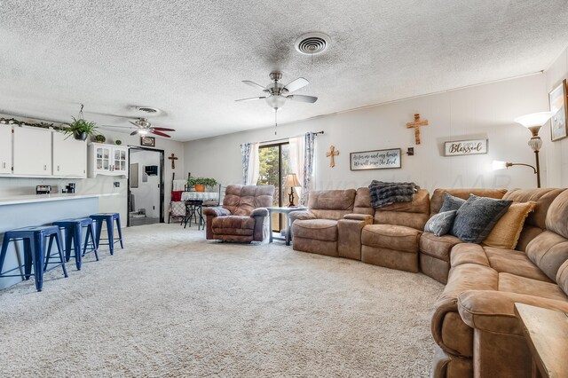 living room featuring light carpet, a ceiling fan, visible vents, and a textured ceiling