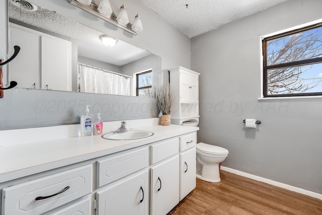bathroom featuring wood finished floors, toilet, vanity, baseboards, and a textured ceiling