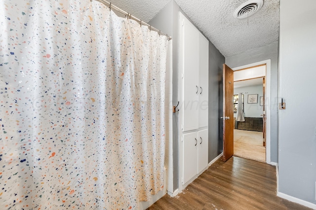 hall with baseboards, wood finished floors, a textured ceiling, and visible vents