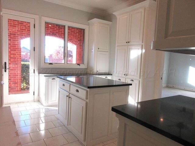 kitchen with white cabinetry, light tile patterned floors, a center island, and crown molding