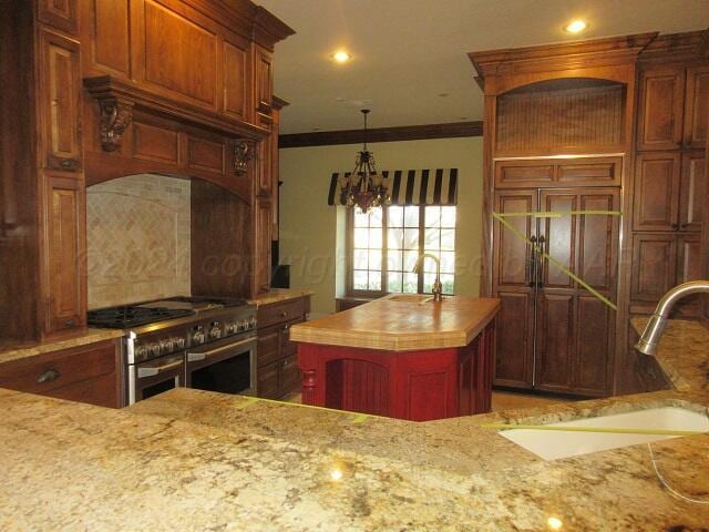 kitchen with light stone countertops, a kitchen island, double oven range, sink, and ornamental molding