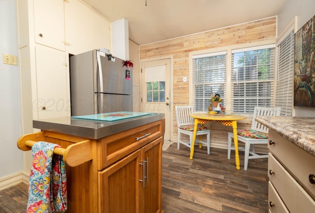 kitchen featuring freestanding refrigerator, stainless steel counters, wooden walls, dark wood finished floors, and white cabinets