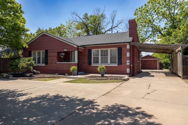 single story home featuring concrete driveway, an outbuilding, a chimney, a carport, and a shingled roof