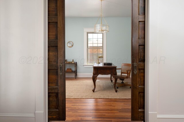 hall featuring wood-type flooring and a notable chandelier