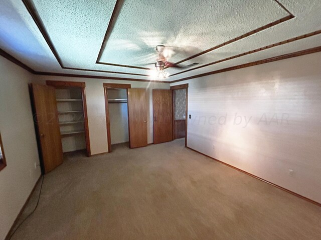 unfurnished bedroom with light colored carpet, a textured ceiling, two closets, and ceiling fan