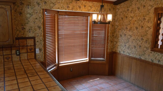 unfurnished dining area with a notable chandelier, light tile patterned floors, and wooden walls