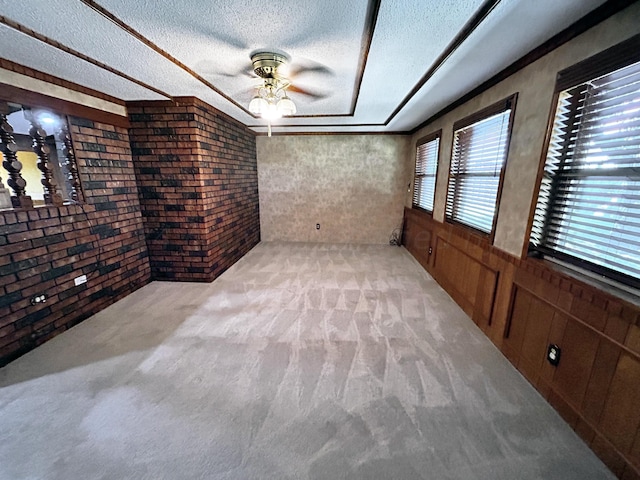 carpeted spare room featuring ceiling fan, a textured ceiling, and brick wall