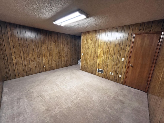 basement featuring carpet flooring, a textured ceiling, and wooden walls