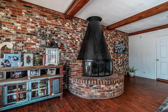 unfurnished living room featuring brick wall, a wood stove, hardwood / wood-style floors, and beamed ceiling