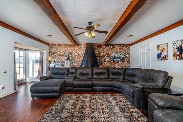 living room with a textured ceiling, dark wood-type flooring, beam ceiling, and ceiling fan