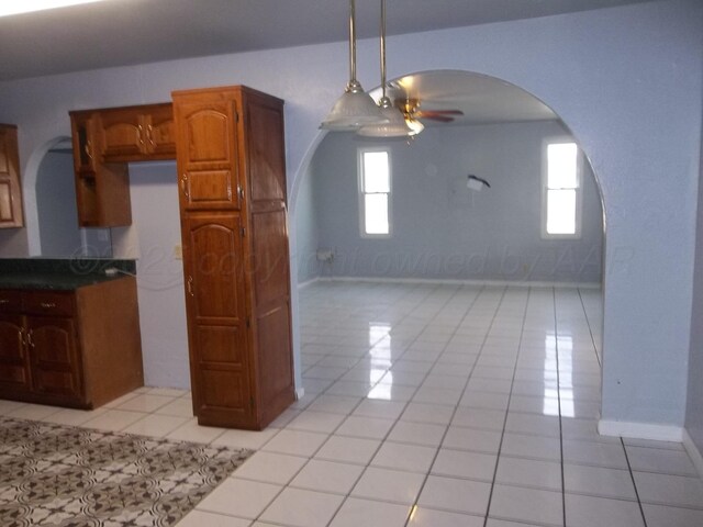 805 Brevard St, Hereford, TX 79045 - kitchen featuring arched walkways, ceiling fan, light tile patterned floors, dark countertops, and brown cabinetry
