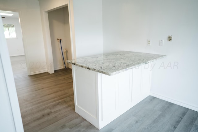 kitchen featuring light stone countertops, dark hardwood / wood-style floors, kitchen peninsula, and white cabinets