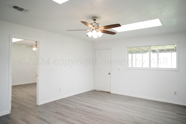 empty room featuring hardwood / wood-style floors, a skylight, and ceiling fan