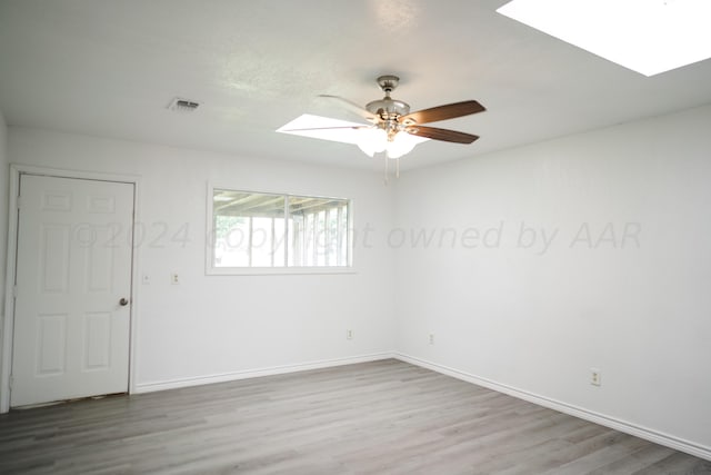 empty room with hardwood / wood-style flooring, ceiling fan, and a skylight