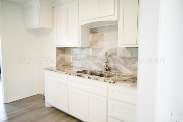 kitchen with tasteful backsplash, white cabinetry, sink, and light stone countertops