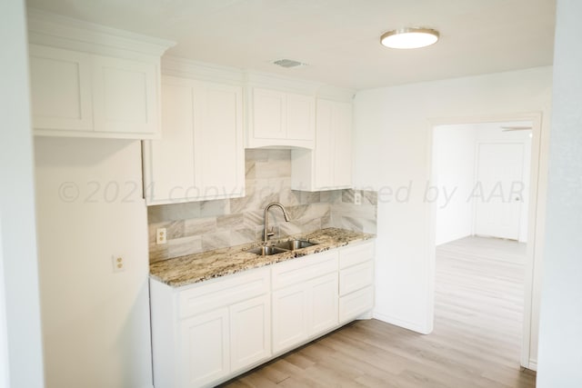 kitchen featuring white cabinetry, sink, light stone countertops, decorative backsplash, and light wood-type flooring