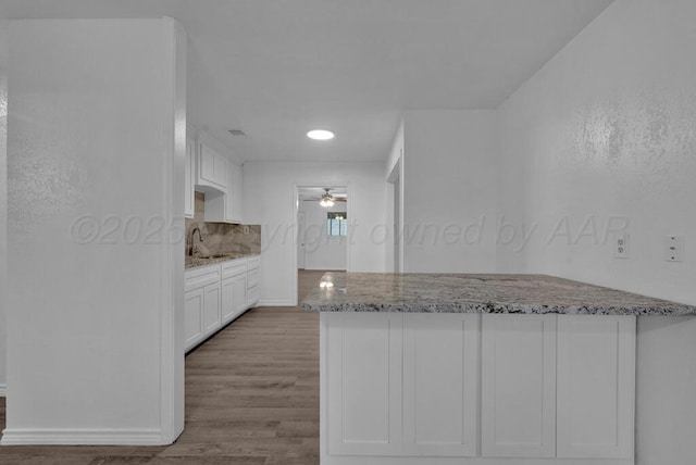 301 Estireno St, Borger, TX 79007 - kitchen featuring a sink, wood finished floors, a ceiling fan, white cabinets, and light stone countertops