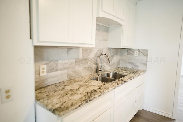 kitchen with backsplash, sink, dark hardwood / wood-style flooring, light stone counters, and white cabinetry