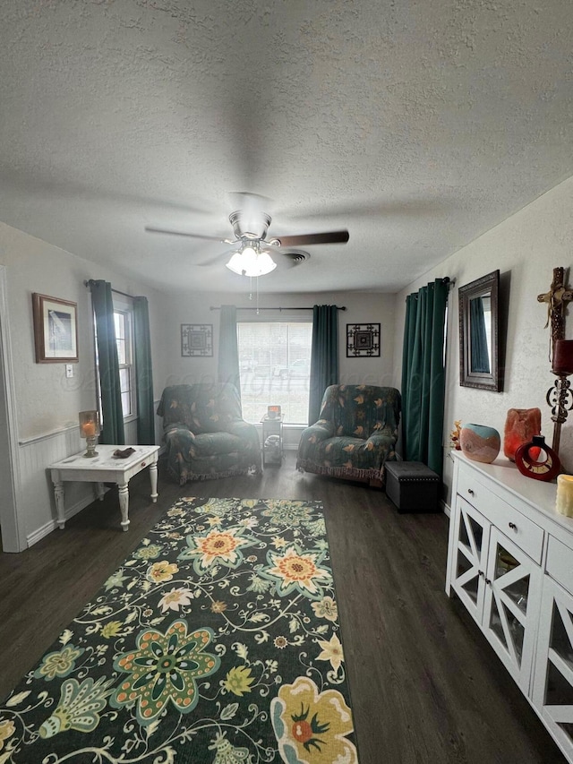 living room featuring dark wood-style floors, a wainscoted wall, a textured ceiling, and a ceiling fan