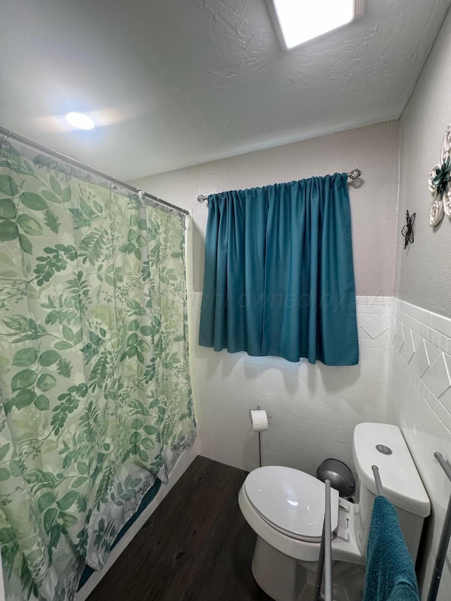 bathroom featuring tile walls, toilet, wainscoting, a textured ceiling, and wood finished floors