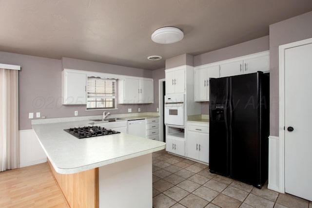 505 Alamo St, Claude, TX 79019 - kitchen featuring black appliances, light countertops, a peninsula, a sink, and white cabinetry