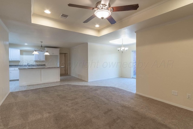 unfurnished living room with ceiling fan with notable chandelier, a raised ceiling, crown molding, and light carpet