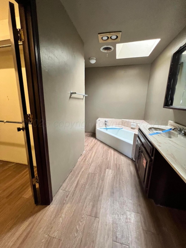 bathroom featuring vanity, a skylight, hardwood / wood-style floors, and a tub