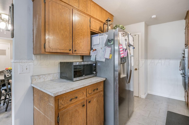 kitchen with light countertops, backsplash, brown cabinetry, and appliances with stainless steel finishes