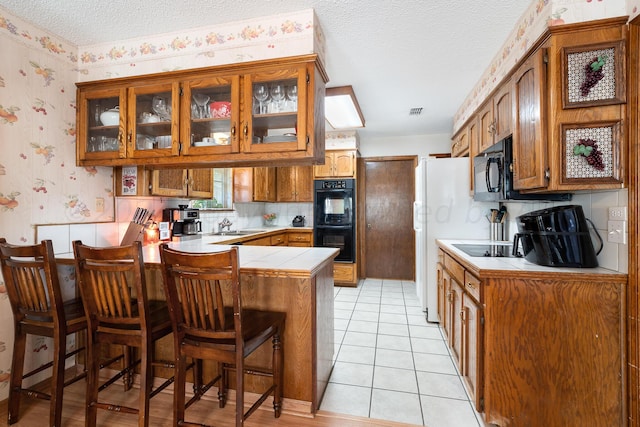 kitchen with a kitchen bar, kitchen peninsula, black appliances, a textured ceiling, and light tile patterned flooring