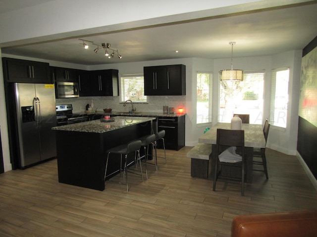 kitchen featuring a kitchen island, appliances with stainless steel finishes, a breakfast bar, pendant lighting, and light hardwood / wood-style floors