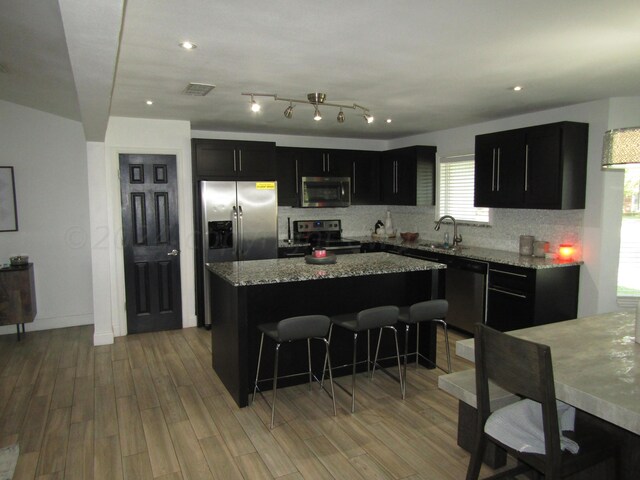 kitchen featuring sink, light stone counters, tasteful backsplash, a center island, and stainless steel appliances