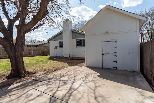 back of house featuring a patio area, a lawn, a chimney, a fenced backyard, and an outdoor structure