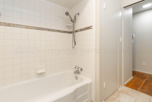 full bath featuring wood finished floors, baseboards, and washtub / shower combination