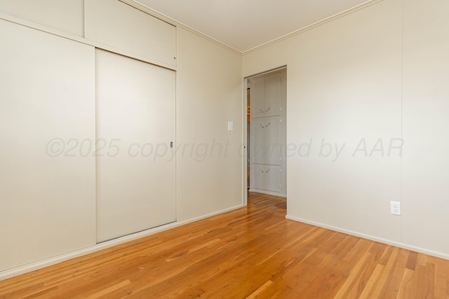 unfurnished bedroom with a closet, light wood-style flooring, baseboards, and ornamental molding
