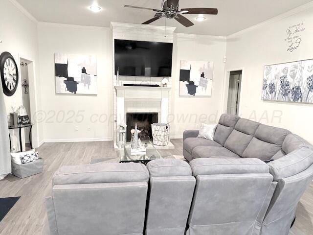 living area featuring crown molding, ceiling fan, wood finished floors, and a large fireplace