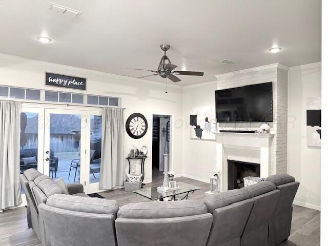 living area featuring crown molding, a large fireplace, a ceiling fan, baseboards, and wood finished floors