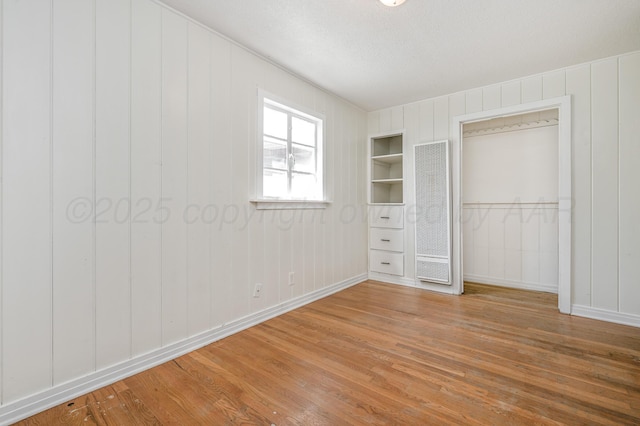 unfurnished bedroom featuring a decorative wall, baseboards, and wood finished floors