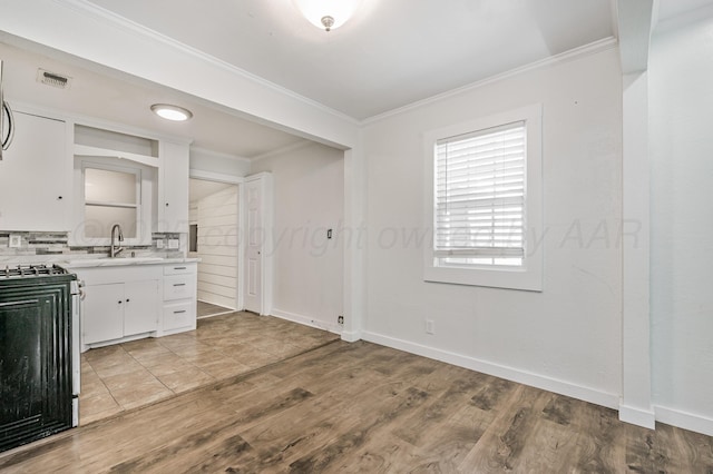 kitchen featuring a sink, gas range oven, light countertops, and ornamental molding