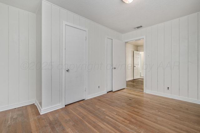 unfurnished bedroom with a decorative wall, visible vents, hardwood / wood-style flooring, and baseboards