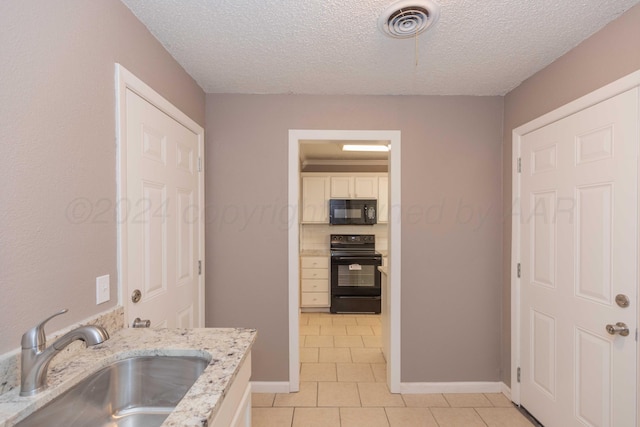 kitchen with light stone counters, a textured ceiling, sink, black appliances, and light tile patterned floors